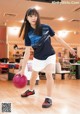 A young woman holding a red bowling ball in a bowling alley.