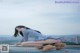 A woman in a blue shirt and pink panties crouching on a ledge.