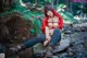 A woman in a red hooded outfit sitting on a rock in the woods.