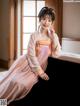 A woman in a pink and orange hanbok sitting on a couch.